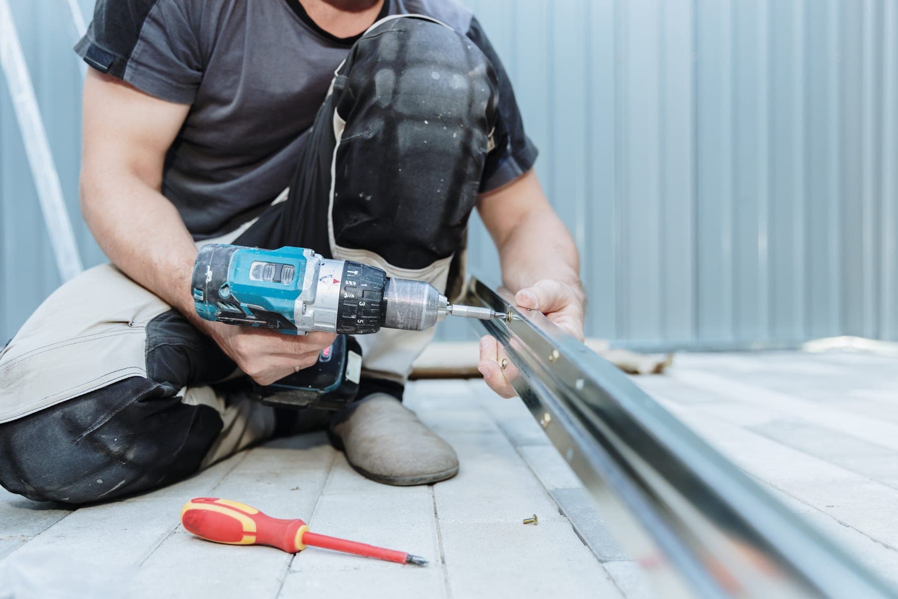 Roof plumber fixing a metal roof panel with a cordless drill
